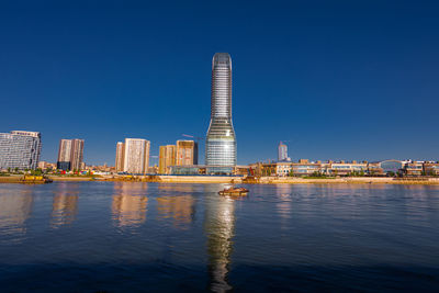 Buildings by river against clear blue sky