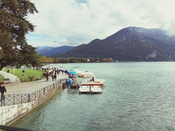 People walking by lake against cloudy sky