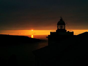 Silhouette lighthouse by sea against sky during sunset