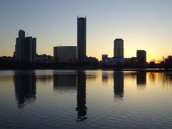 Scenic view of lake by buildings against sky during sunset