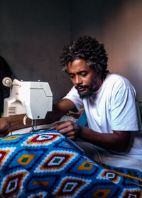 Young man sewing cloth at home