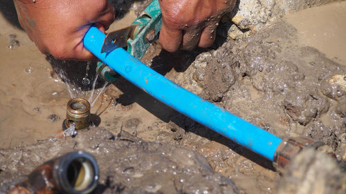 Cropped hands of man repairing pipe in mud