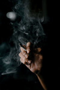 Midsection of man smoking cigarette against black background