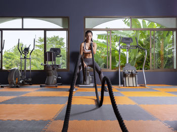 Athletic woman exercising with battle ropes at gym