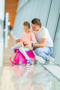 Father holding girl sitting on toy in corridor