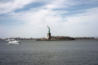 Statue of liberty in city against cloudy sky