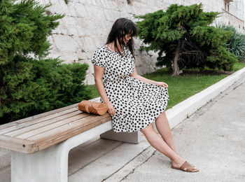 Portrait of attractive young woman in summer polka-dot dress sitting on bench.