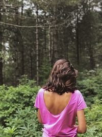 Rear view of woman standing against trees in forest