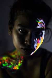 Close-up portrait of young woman with face paint in darkroom