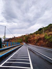 Empty road along trees and against sky