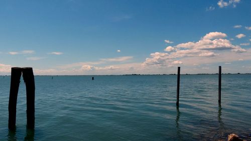 Wooden posts in sea against sky