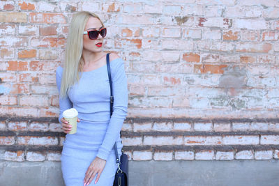 Beautiful woman holding coffee cup whiles standing by wall outdoors