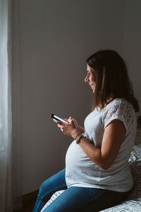 Young pregnant woman at home using mobile phone