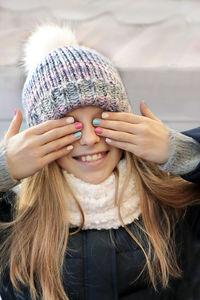 Smiling girl covering eyes with hands outdoors