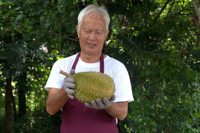 Man holding fruit while standing against trees