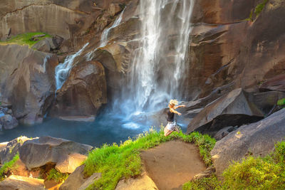 High angle view of woman jumping against waterfall