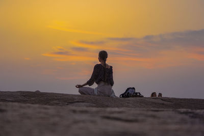 People sitting on rock at beach against sky during sunset