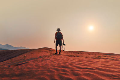 Rear view of man walking at desert against sky during sunset