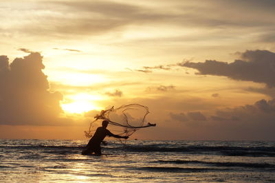 Silhouette fishing net on sea against sky during sunset