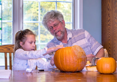 Grandpa watches as a child draws a face on a pumpkin for him to carve