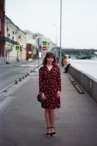 Portrait of woman standing on sidewalk against sky in city