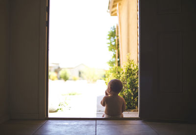 Rear view of baby sitting on doorway during sunny day