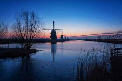 Traditional windmill by river against sky during sunset