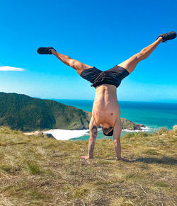 Full length rear view of young man with arms raised against sky