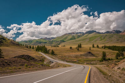 Empty road leading towards mountains against cloudy sky