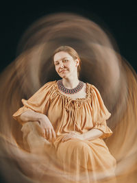 Portrait of young woman standing against black background