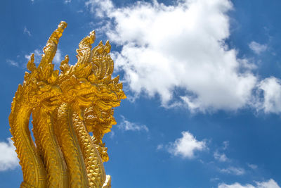 Low angle view of golden statue against cloudy sky