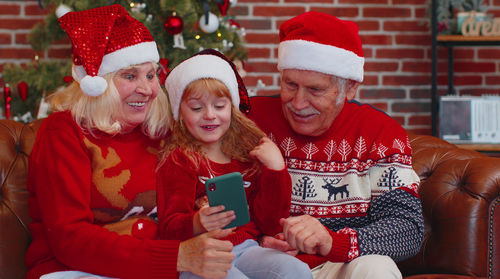 Smiling grandparent with granddaughter using phone at home