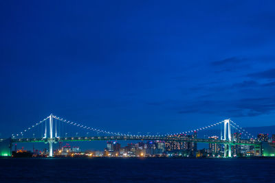 Illuminated bridge over sea against sky at night