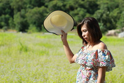 Woman holding hat while standing on field