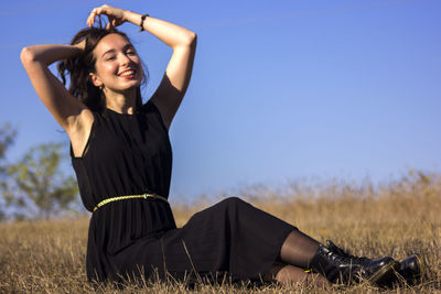 Low angle view of young woman sitting on grassy field against clear sky