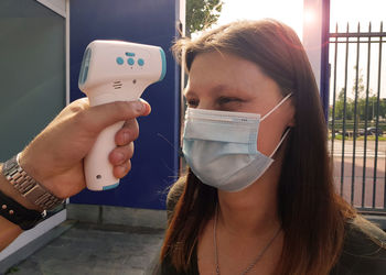 Cropped hand of man holding infrared thermometer against woman