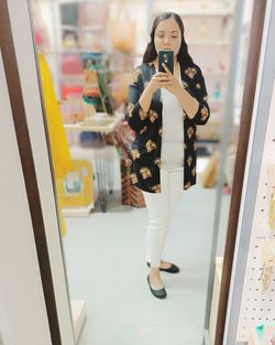 Full length of young woman using mobile phone in store