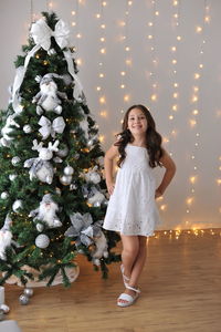 Portrait of smiling young woman standing against christmas tree