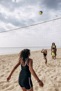 Rear view of girl playing volleyball with family at beach