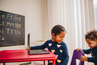 Baby boy pushing chair of sister studying at home