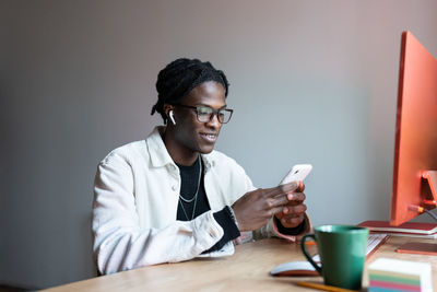 Joyful carefree african american man in headphones use phone to switch playlist sits at office desk