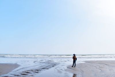 Woman using mobile phone at beach against clear sky