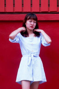 Portrait of a beautiful young woman standing against red wall