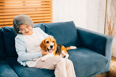 Young woman with dog sitting on sofa at home