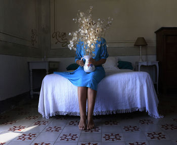 Full length of woman sitting on bed at home