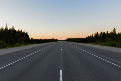 Road by trees against sky during sunset