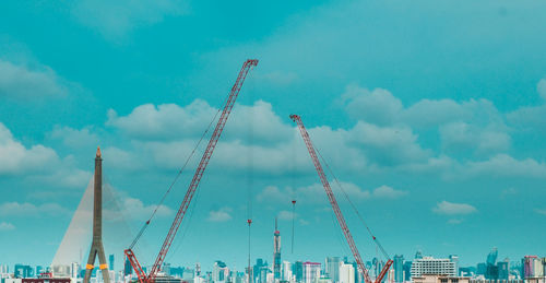 Low angle view of cranes against buildings in city