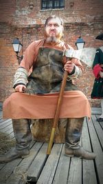 Man in executioner costume looking away while sitting against building