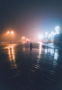 Illuminated street by sea against sky at night