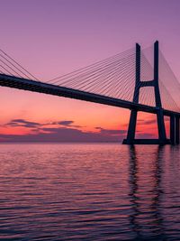 Suspension bridge over sea against sky during sunset